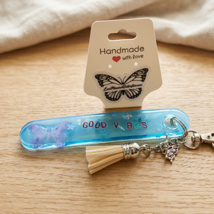 Handmade blue resin keychain with words "Good Vibes" and cream colored tassel.
